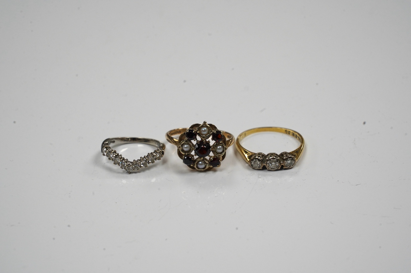 Two 18ct gold and diamond set rings including chevron shape and a 9ct gold, garnet and seed pearl set ring. Condition - fair